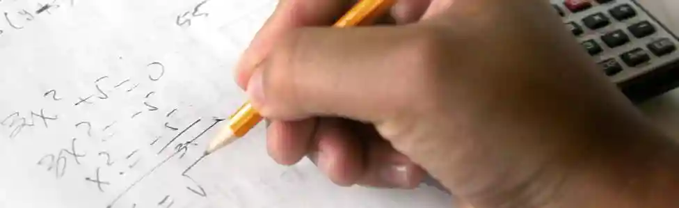 A hand holding a pencil working on math problems